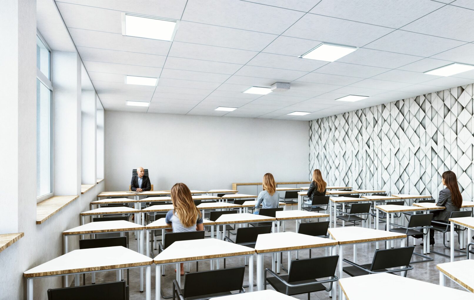 Modern classroom interior with minimalist white walls, geometric textured feature wall, and large windows providing natural light. The room features black chairs and triangular white desks arranged in rows, with a lecturer seated at the front and several students spaced out across the room.
