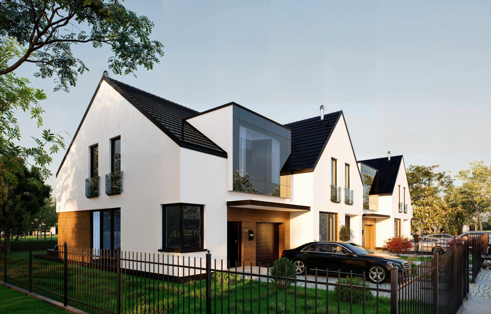 A modern suburban housing development featuring white gable-roofed buildings with dark accents, large windows, and fenced front gardens. The visuals capture different angles of the row houses set against a soft blue sky and cobblestone street with people walking, cars parked, and lush greenery enhancing the residential atmosphere.